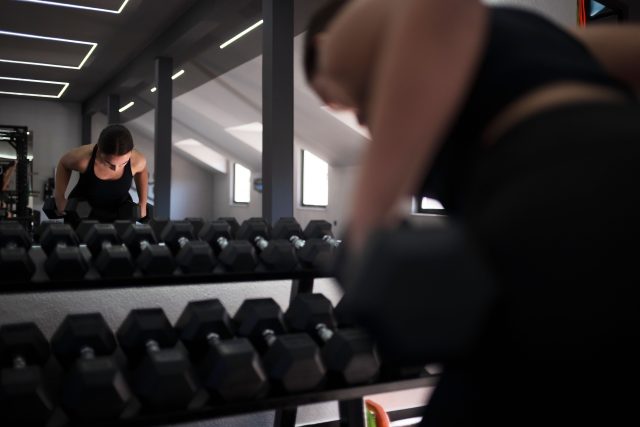 A woman focuses on her workout while lifting dumbbells in a bright gym