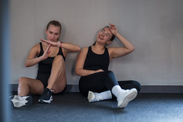 Two women sit on the gym floor, taking a break after exercising