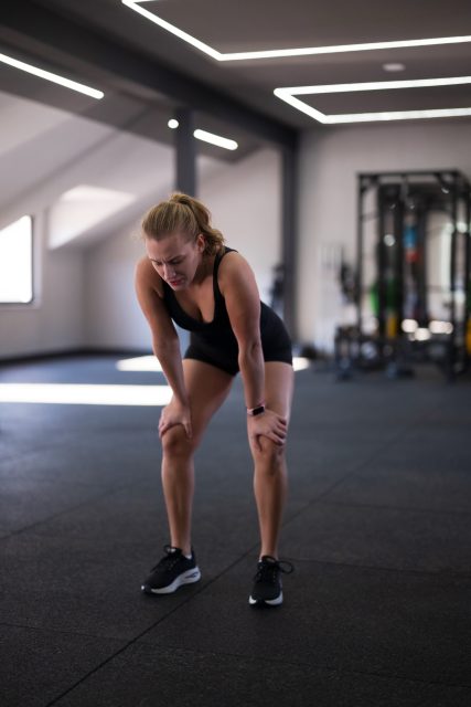 A focused woman takes a moment to recover after a demanding workout in a bright, spacious gym