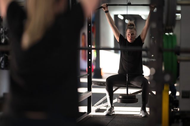 In a vibrant gym, a woman focuses on lifting weights while seated on a bench