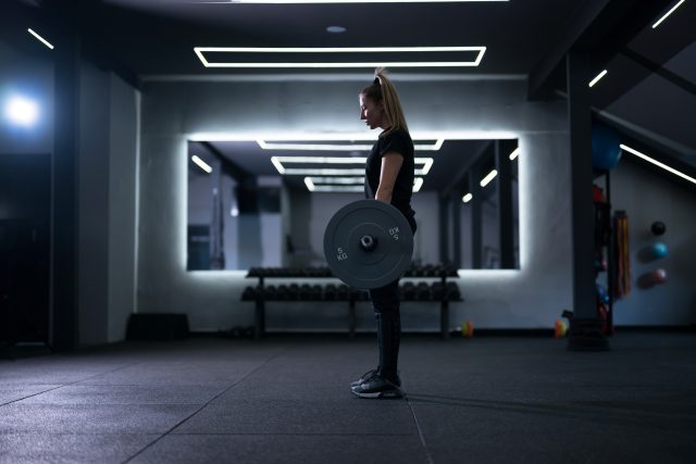 A woman stands focused, lifting a barbell in a stylish gym