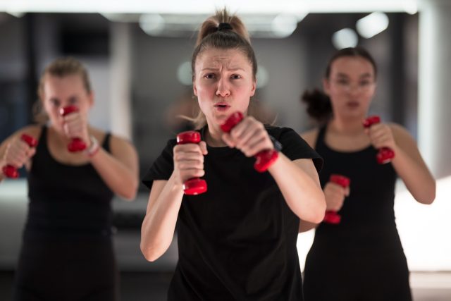 Group of women are actively participating in a fitness class, focused on their workout with small dumbbells