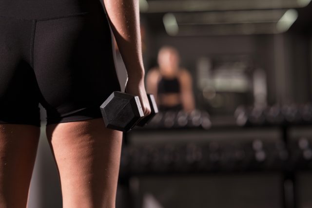 A woman holds a dumbbell in her right hand while preparing to lift in a sleek gym