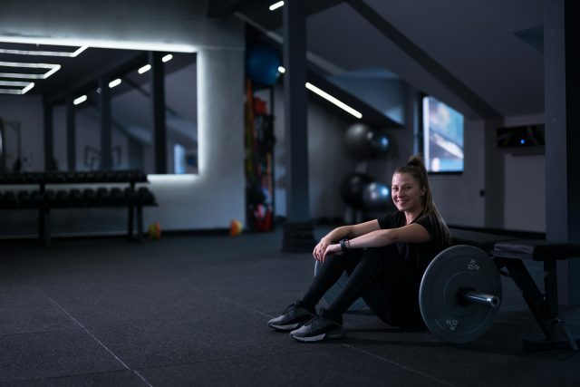 A young woman relaxes against a barbell after an intense workout in a stylish gym