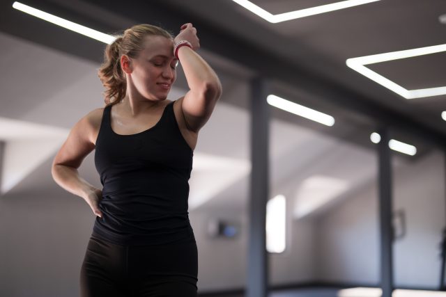 A young woman in black athletic wear wipes her forehead while taking a break in a sleek gym