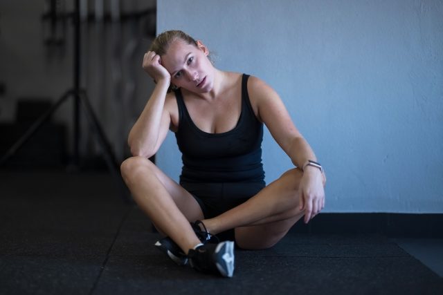 A woman sits on the gym floor, showing tiredness after an intense workout session