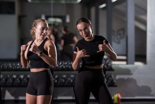 Two young women are posing playfully in a gym, enjoying their workout together