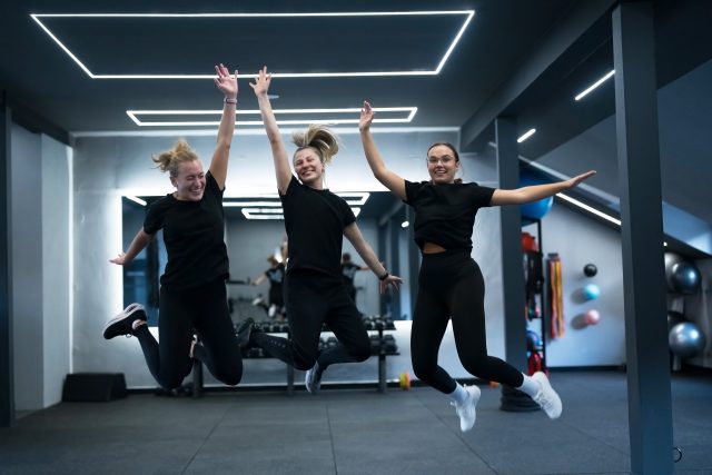 Group of women dressed in black workout clothes jump energetically in a modern gym