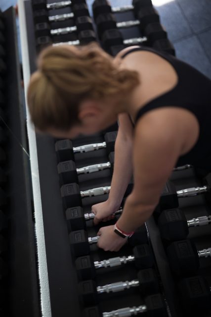 A woman is sorting and arranging dumbbells in a gym
