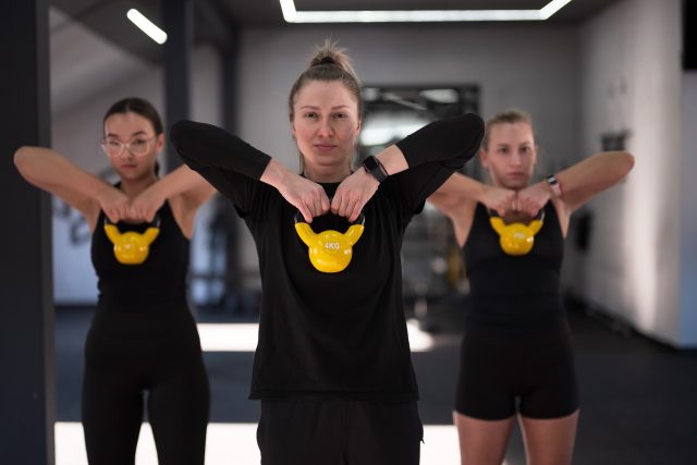 Group of women in black workout attire perform kettlebell exercises in a sleek gym