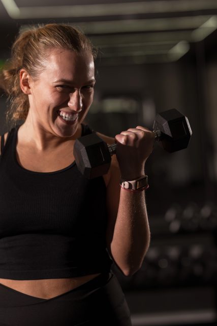 A young woman smiles while lifting a dumbbell in a gym