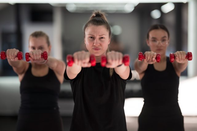 Group of women participate in an intense workout session at a gym, focusing on strength training