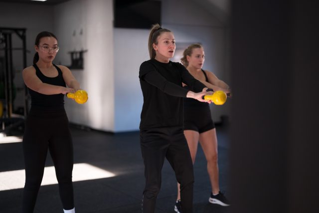 Group of women are training with kettlebells in a well-lit fitness studio