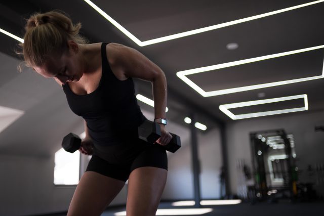 A person engaged in strength training exercises using dumbbells in a sleek gym space with natural light