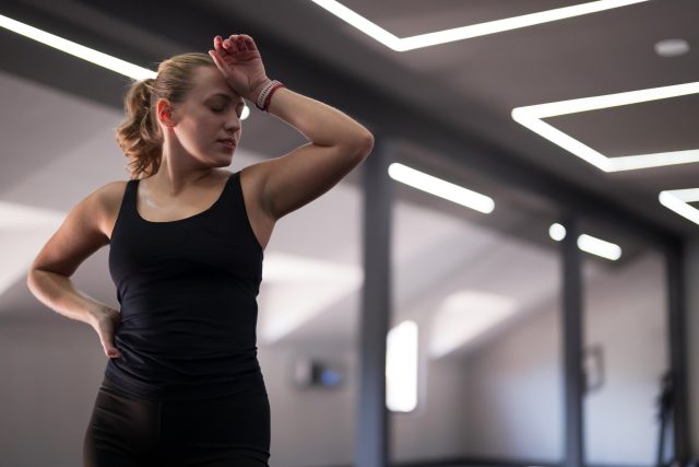 A fitness enthusiast wipes sweat from her forehead while taking a break from her workout