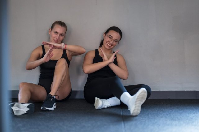 Two friends take a break in the gym, sitting on the floor in exercise attire