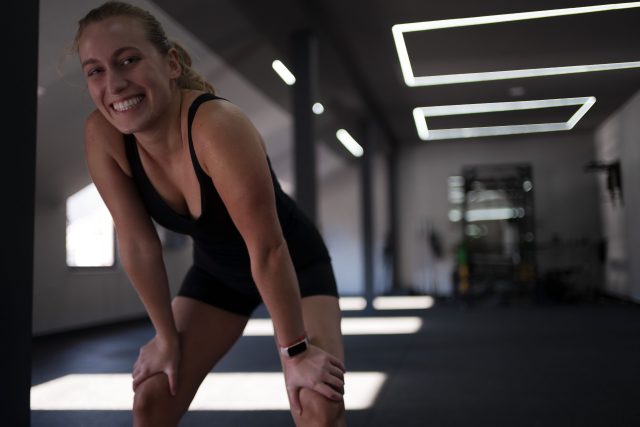 A woman in athletic gear leans forward with her hands on her knees, catching her breath