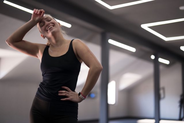 A woman smiles with joy after completing her workout in a bright fitness studio
