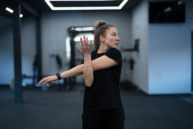 A woman is performing an arm stretch in a sleek gym