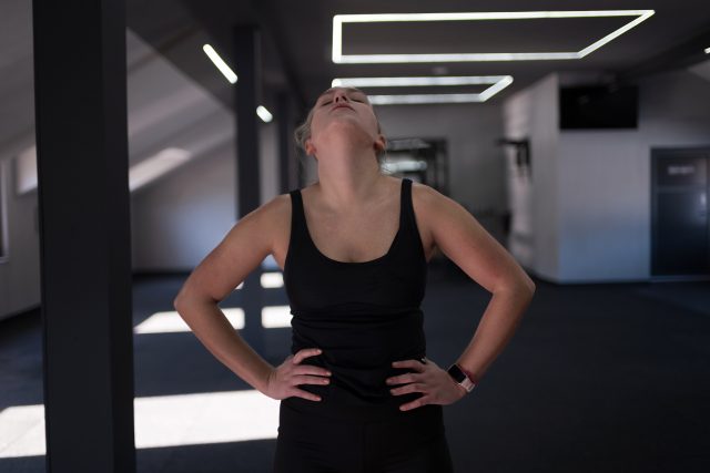 A woman stands confidently in a gym, wearing athletic gear