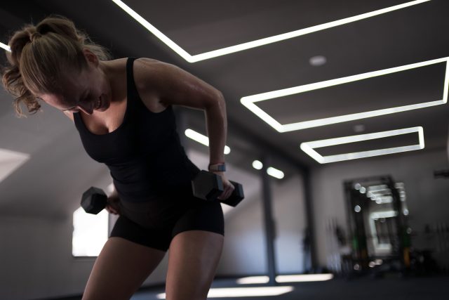 A woman performs a strength training exercise using dumbbells in a modern fitness studio