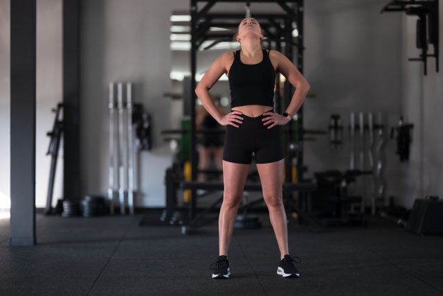 In a contemporary gym, a young woman takes a moment to breathe deeply during her workout