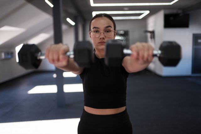 A woman lifts dumbbells in a well-lit gym, focusing on her workout