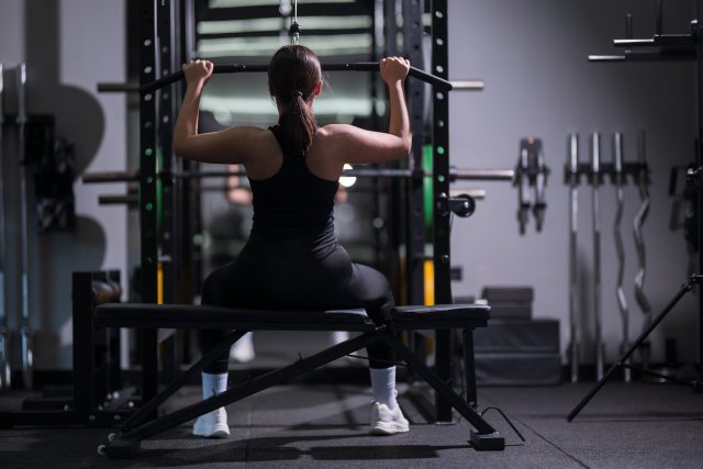 A woman is exercising in a gym, focused on lifting weights on a barbell