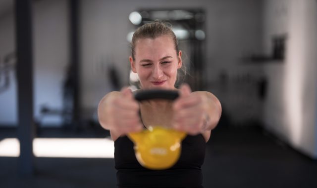 A young woman is engaged in a workout using a kettlebell, showing determination and focus in a gym setting