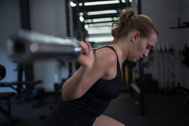 A woman is focused as she performs a barbell squat in a well-equipped gym