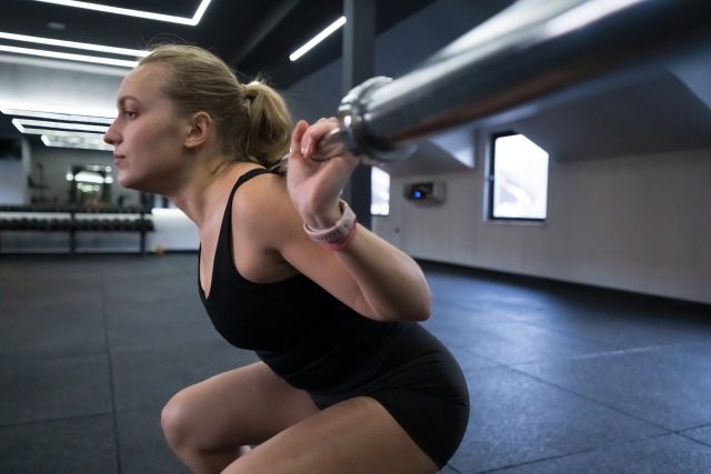 A woman is engaged in a squat exercise while lifting a barbell in a contemporary gym