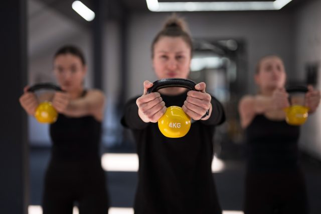 Group of women perform kettlebell exercises in a well-lit gym