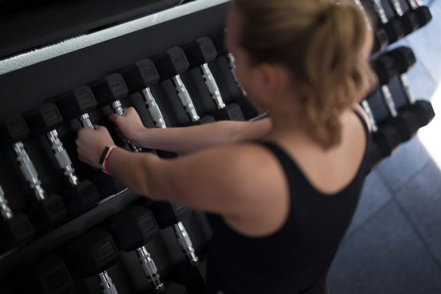 A woman in workout attire is reaching for dumbbells in a gym