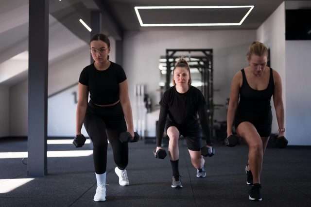Group of women are performing lunges with dumbbells in a contemporary gym